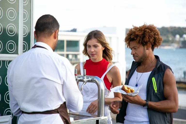 Un serveur prend la commande de deux clients sur une terrasse au bord de l'eau