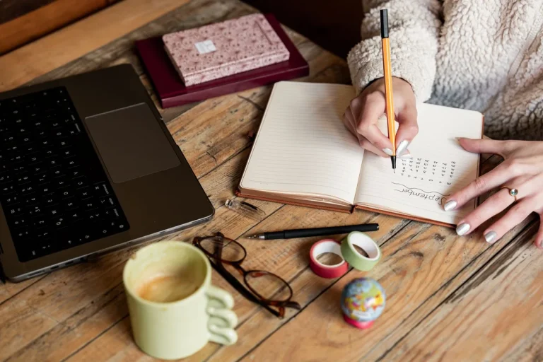 Une personne note dans un carnet à côté d'un ordinateur portable et d'une tasse de café
